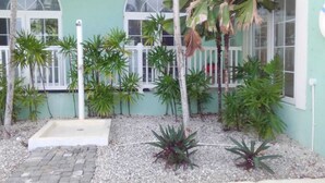 Um pequeno espaço ao ar livre com um caminho pavimentado, um jardim com diversas plantas e um cercado branco.