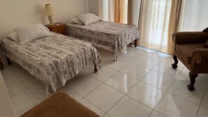 Quarto de hotel com duas camas, um sofá, uma lâmpada e uma janela com cortinas.
