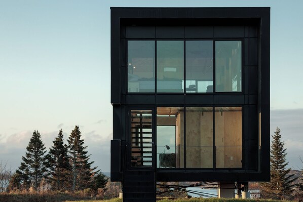 A modern, multi-level cabin with large windows, a wooden interior, and a view of the surrounding landscape.