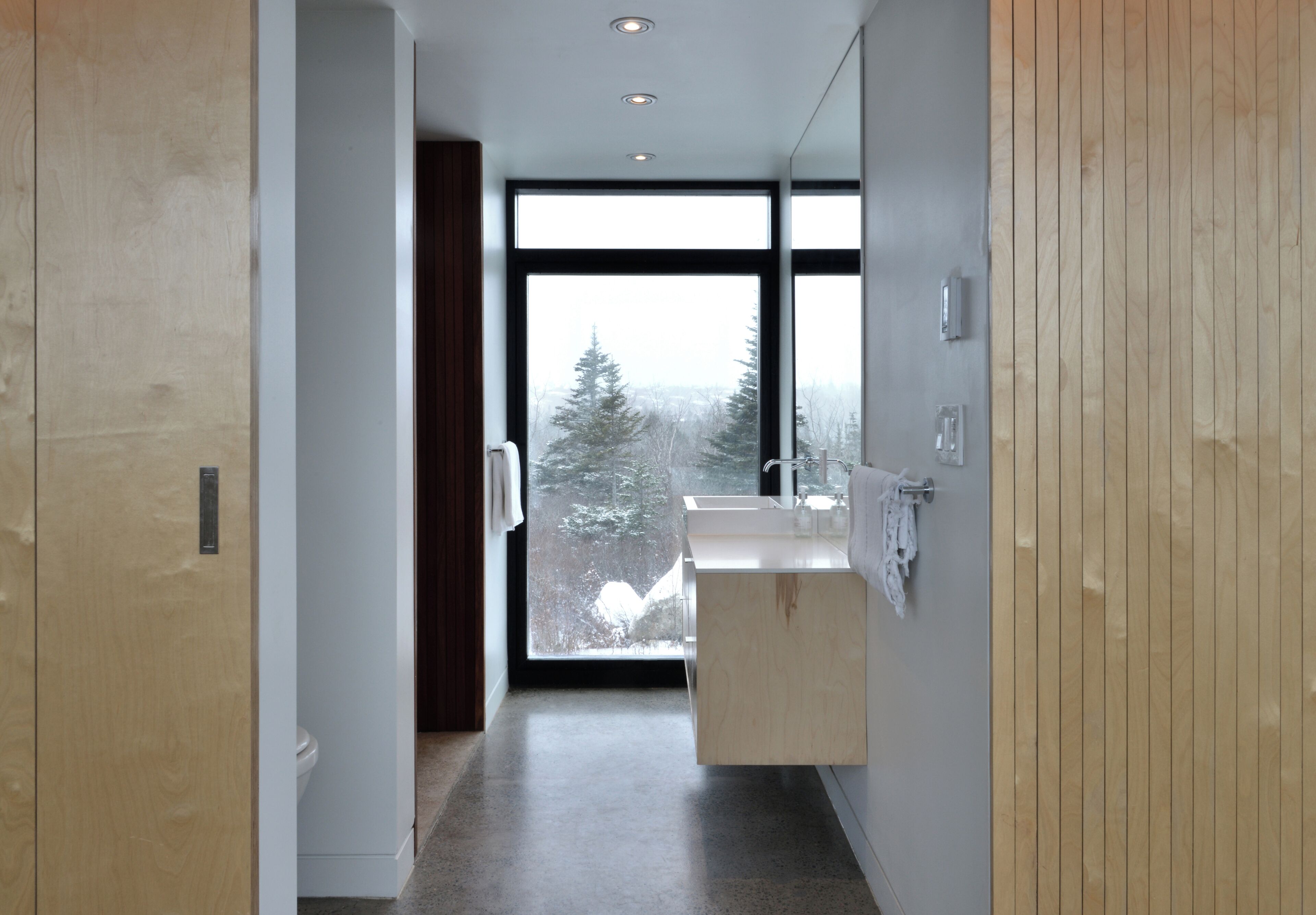 Un bagno moderno con un'ampia finestra, un mobile bagno in legno e uno specchio.