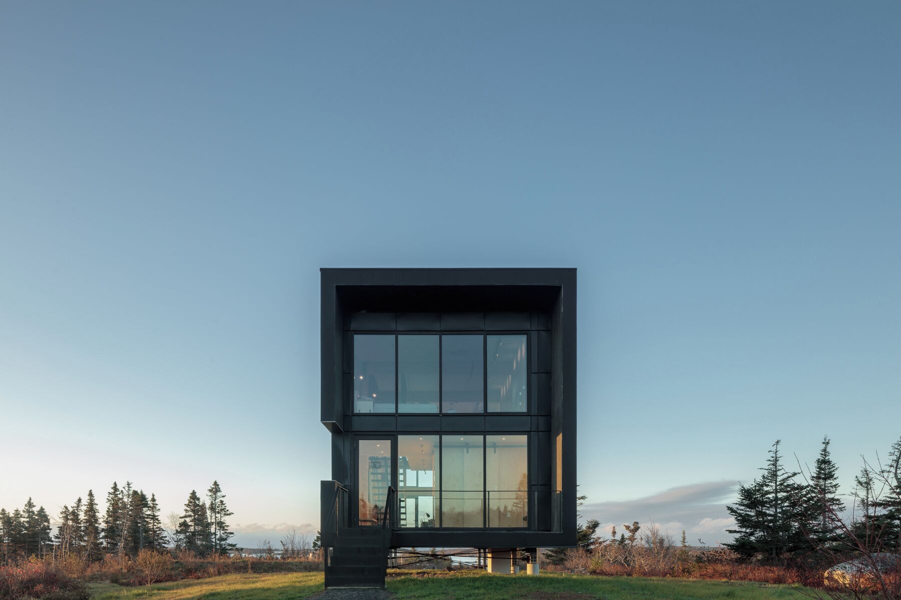 Un bâtiment moderne de forme rectangulaire, doté de grandes fenêtres, et entouré d’un paysage naturel avec des arbres et un ciel dégagé.