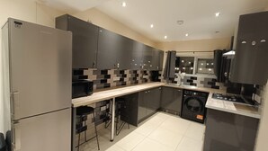 A modern kitchen with a built-in washing machine, a microwave, and a stove. - Triplex Hot Tub House with Private Garden (Cardiff)
