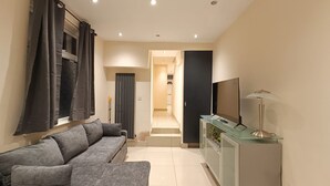 A modern living room with a grey sofa, a glass TV stand, and a flat-screen TV. - Triplex Hot Tub House with Private Garden (Cardiff)