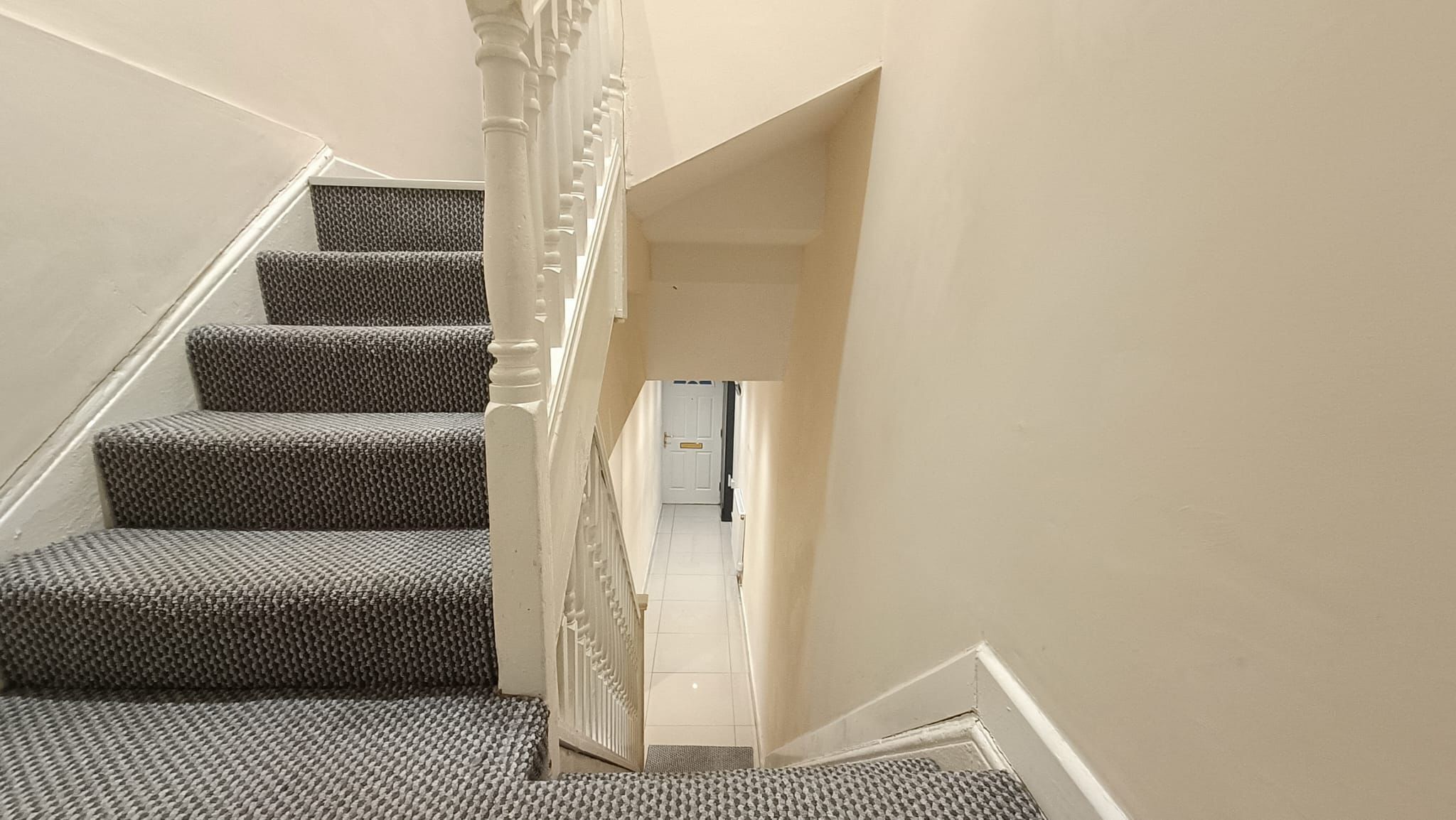 A staircase with carpeted steps and white balusters, leading to a landing with a door.