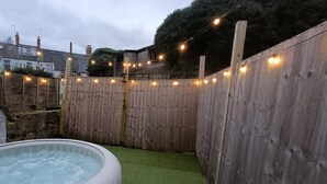 A backyard with a hot tub, artificial grass, and a wooden fence. - Triplex Hot Tub House with Private Garden (Cardiff)