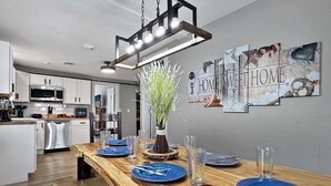 A modern kitchen with white cabinets, a wooden dining table set with blue plates and clear glasses, and a decorative vase with greenery. - Two Homes walk to Convention Ctr Hot Tub Game room (Branson)