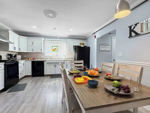 A modern kitchen with white cabinets, a black refrigerator, and a dining table set with fruits and vegetables. - Two Homes walk to Convention Ctr Hot Tub Game room (Branson)