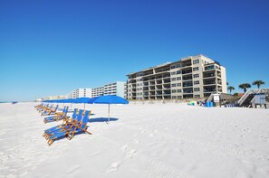 Een strand met rijen blauwe parasols en ligstoelen, een meerlaags hotel en palmbomen op de achtergrond.