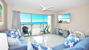 A living room with a sofa, a coffee table, and a TV. There is a balcony with a view of the ocean. - Emerald Towers West • Beach Front • Ocean View • Beach Service etw3003 (Fort Walton Beach)