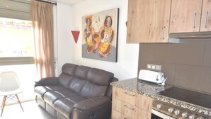 Eine moderne Küche mit Einbauofen und Toaster, ein braunes Ledersofa, ein Esstisch mit Stuhl und ein Bild an der Wand.