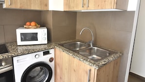 Eine kompakte Küche mit Holzschränken, einer eingebauten Mikrowelle, einem Edelstahl-Spülbecken und einer Waschmaschine.