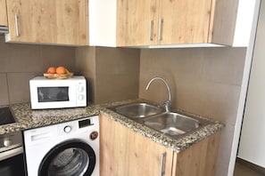 A compact kitchen with wooden cabinets, a built-in microwave, a stainless steel sink, and a washing machine. - Bright apartment in central Roses, just 300 m from the beach. Sleeps 6. Fully equipped and comfortable (Roses)