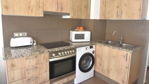 Eine kleine Küche mit Holzschränken, einem eingebauten Ofen, einer Mikrowelle, einer Waschmaschine und einer Arbeitsplatte aus Granit.