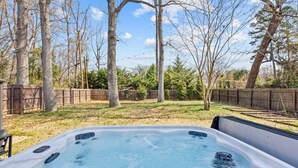 A hot tub in a backyard with a wooden fence and trees. - Spacious Charlotte Retreat with Private Hot Tub (Charlotte)