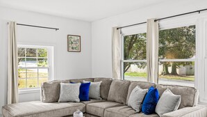 A modern living room with a grey sectional sofa, a round coffee table with decorative vases, and large windows offering a view of the outdoors. - Spacious Charlotte Retreat with Private Hot Tub (Charlotte)