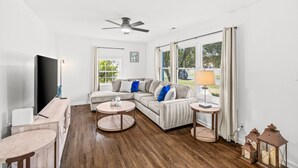 A modern living room with a sectional sofa, a round coffee table, a flat-screen TV, and a ceiling fan. - Spacious Charlotte Retreat with Private Hot Tub (Charlotte)