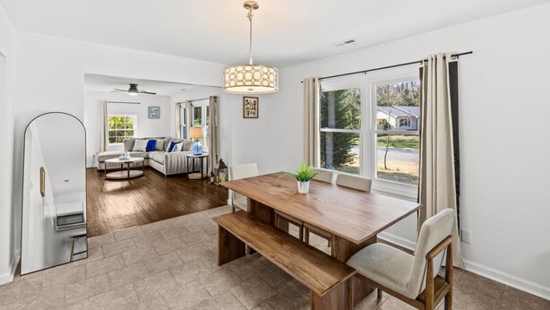 A spacious living area with a wooden dining table, a sofa, and a large window with curtains. - Spacious Charlotte Retreat with Private Hot Tub (Charlotte)