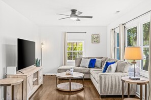 A modern living room with a flat-screen TV, a ceiling fan, a sofa with cushions, a coffee table, and a lamp.