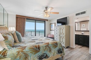 A bedroom with a bed, a ceiling fan, a TV, a dresser, and a bathroom with a mirror. - Watercrest 1101 - Free Beach Chairs! (Panama City)