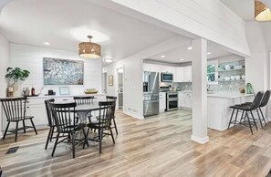 A spacious kitchen with white cabinetry, a dining area with black chairs, and a large island with a sink. - Private Lakefront Retreat with Fire Pit & Sunset Views (Kansasville)