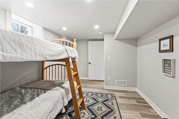 Habitación con literas, una escalera de madera, un tapete estampado y una puerta al fondo.