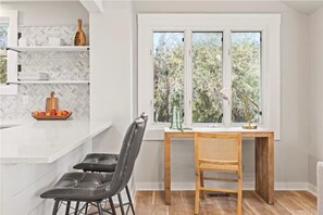 A modern kitchen with a white countertop, a wooden dining table, and a window with a view of trees. - Private Lakefront Retreat with Fire Pit & Sunset Views (Kansasville)
