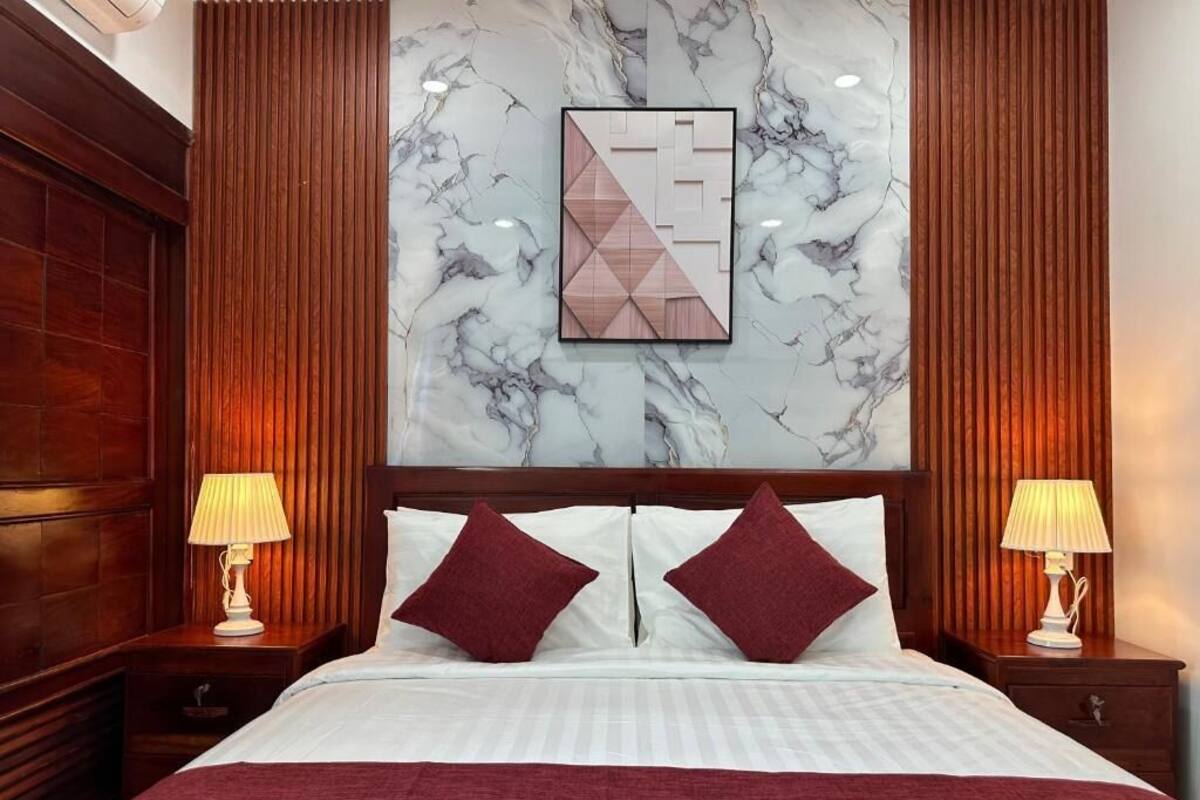 A hotel room with a large bed, two nightstands, a marble-patterned wall, and a geometric artwork above the bed.