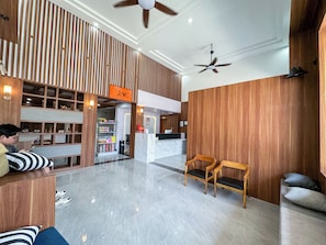 Een hotel lobby met een receptiebalie, een zithoek en een plafondventilator.