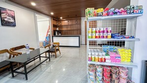 Quarto de hotel com área de refeições, cozinha e prateleira com lanches e artigos de higiene pessoal.