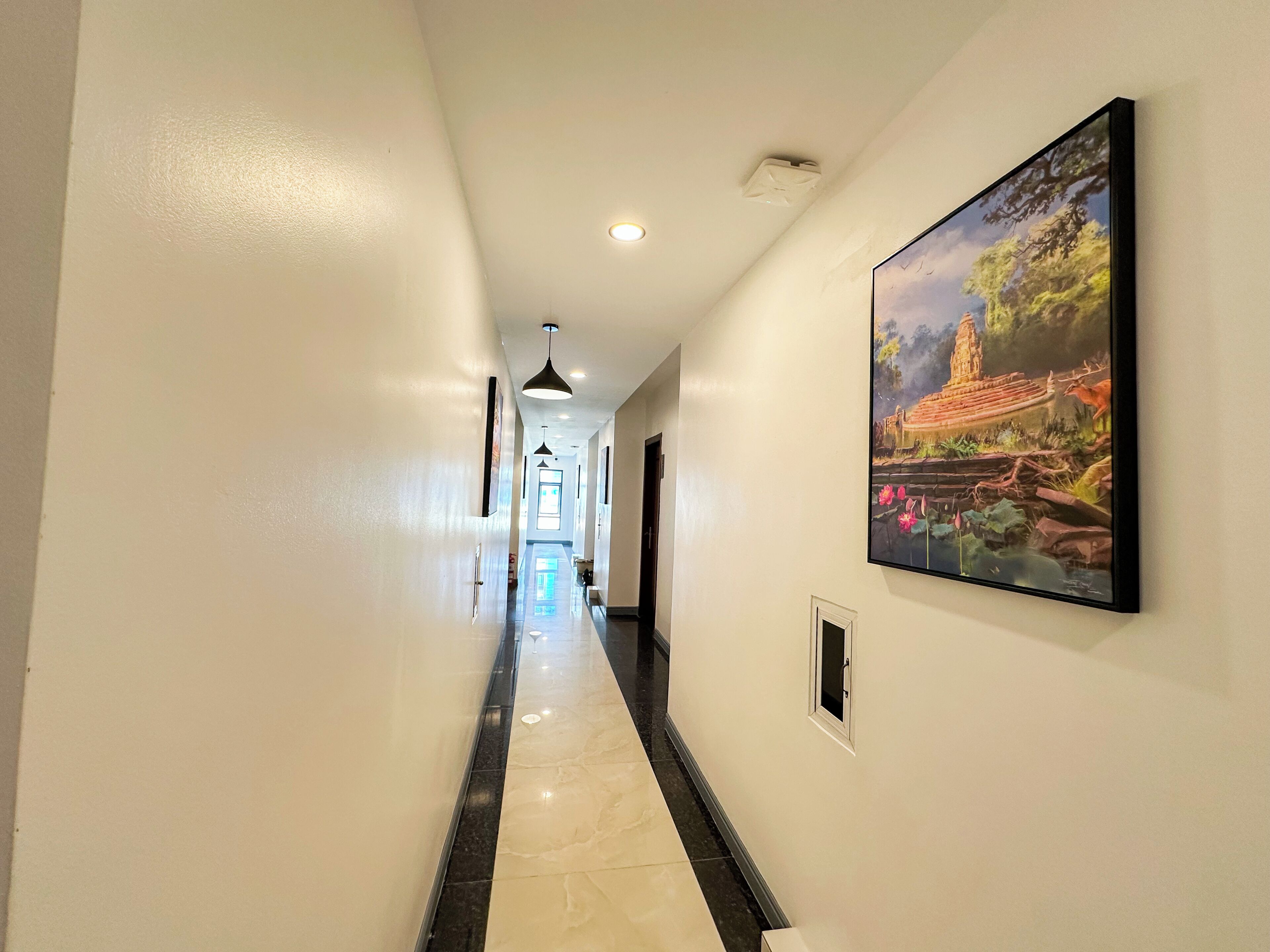 A hotel hallway with a marble floor, a painting on the wall, and a door at the end.