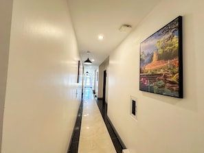 A hotel hallway with a marble floor, a painting on the wall, and a door at the end.