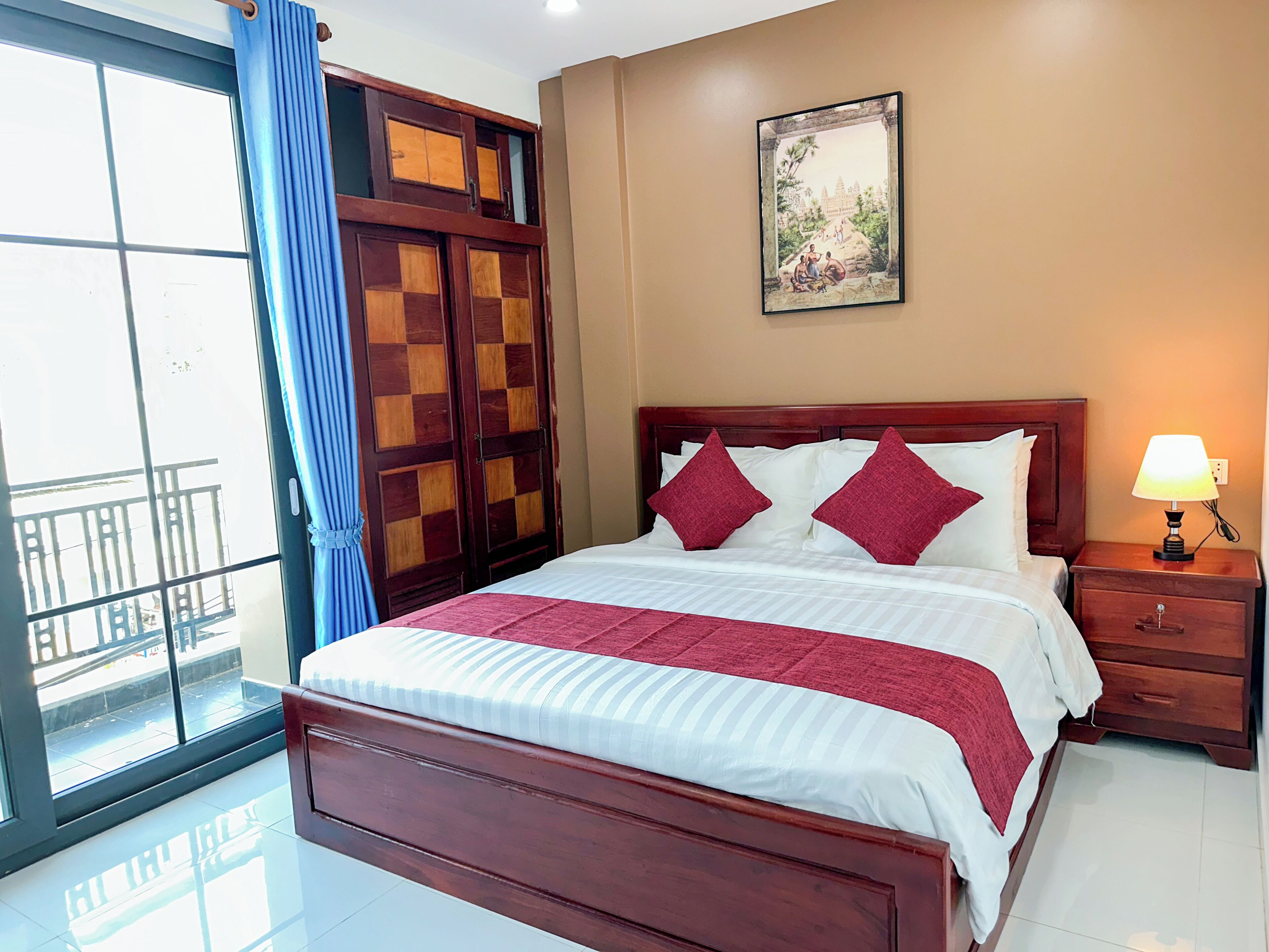 A hotel room with a large bed, a nightstand, a lamp, a window with curtains, and a wall-mounted picture.