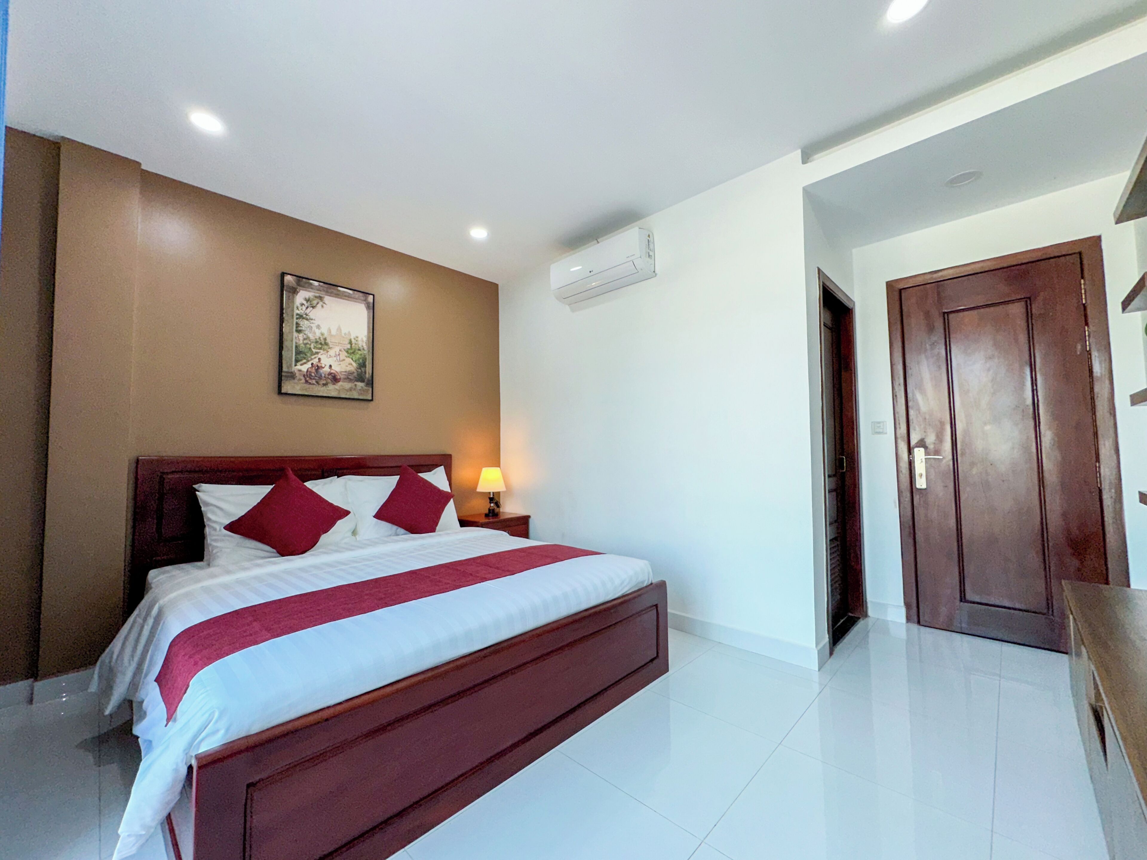 Habitación de hotel con una cama grande, una mesita de noche con lámpara, aire acondicionado en la pared y una puerta que da a otra habitación.
