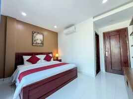 Habitación de hotel con una cama grande, una mesita de noche con lámpara, aire acondicionado en la pared y una puerta que da a otra habitación.