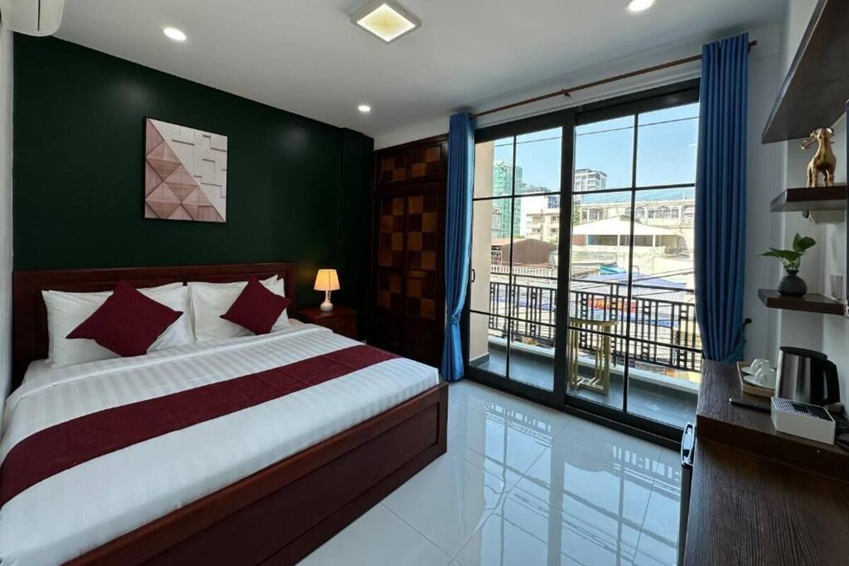 A hotel room with a large bed, a view of the city through the window, and a balcony with a railing.
