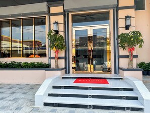 Entrada de un edificio con puerta de vidrio, escalones y un felpudo rojo.