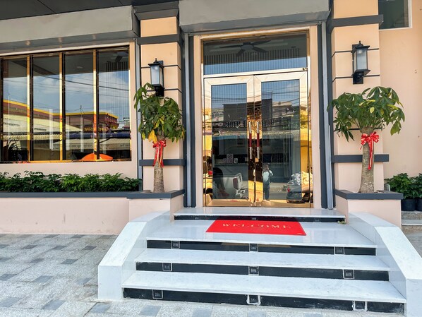 Entrada de un edificio con puerta de vidrio, escalones y un felpudo rojo.