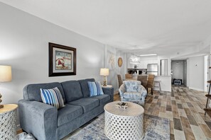 A modern living room with a grey sofa, patterned armchairs, a round coffee table, and a kitchen in the background. - Gulf Front 2/2 Flash sale 3rd floor unit PPE6311 (Gulf Shores)