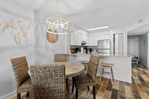 A modern kitchen with white cabinets, a stainless steel refrigerator, and a wooden dining table with wicker chairs. - Gulf Front 2/2 Flash sale 3rd floor unit PPE6311 (Gulf Shores)
