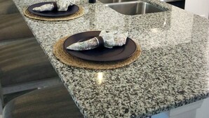 Eine moderne Küche mit Granit Arbeitsplatten, Edelstahlgeräten und weißen Schränken.