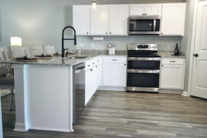 Une cuisine moderne avec des meubles blancs, un plan de travail en granit, des appareils électroménagers en acier inoxydable et un plancher en bois.