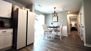 Una cocina moderna con armarios blancos, un refrigerador de doble puerta y un comedor con mesa y sillas.