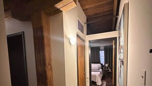 Ein Flur mit Holzboden und -wänden, der zu einem Schlafzimmer mit Bett und Nachttisch führt.