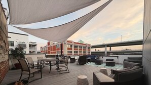 Eine Dachterrasse mit Gartenmöbeln, einer Feuerstelle und Blick auf eine Brücke sowie Gebäude im Hintergrund.