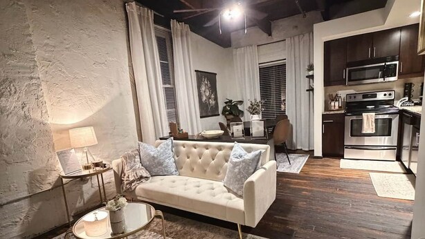 Ein Wohnzimmer mit Sofa, Couchtisch und Teppich; ein Essbereich mit Tisch und Stühlen; sowie eine Küche mit Geräten.