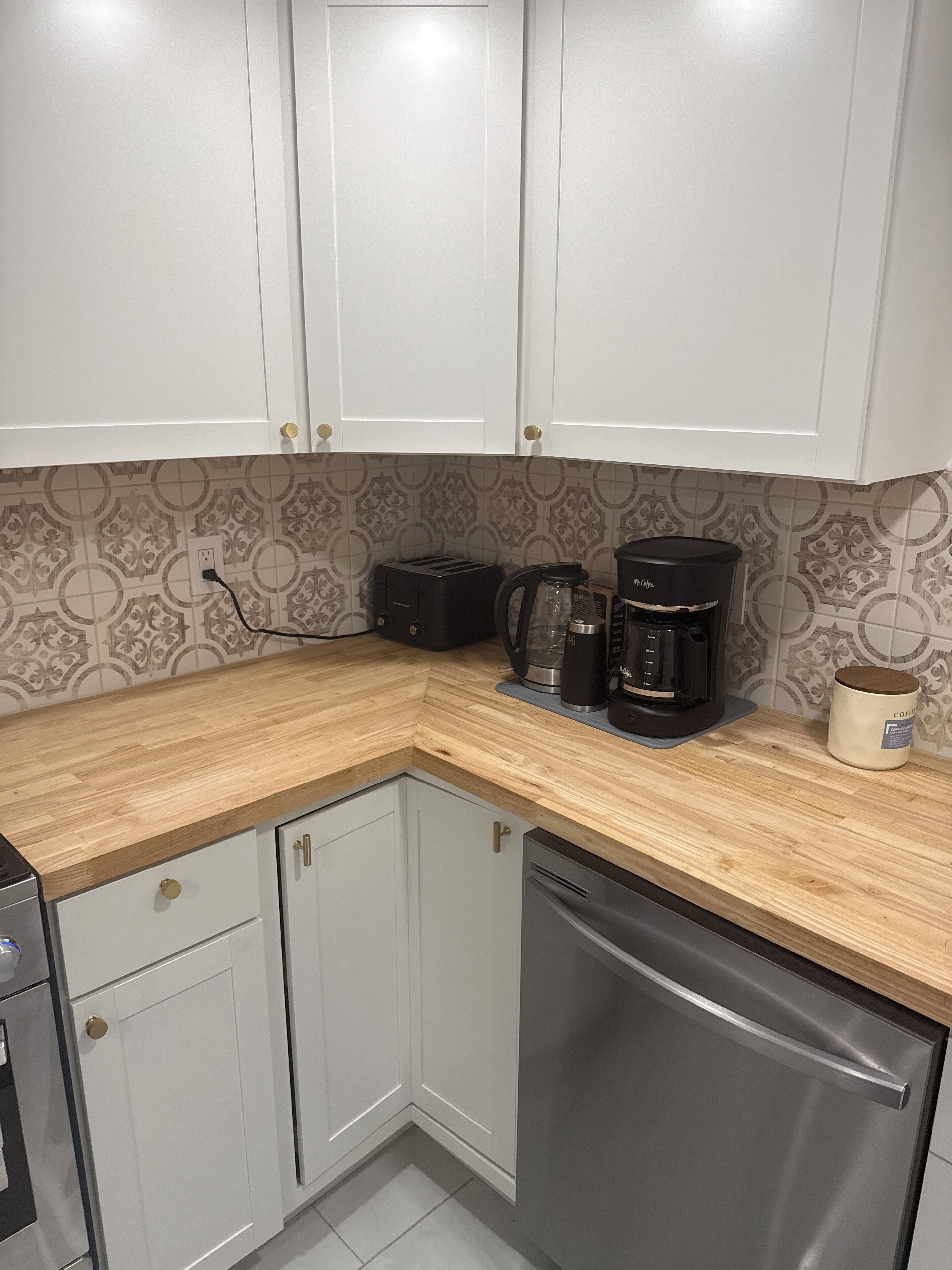 A kitchen with white cabinets, a wooden countertop, a coffee maker, a toaster, and a dishwasher.