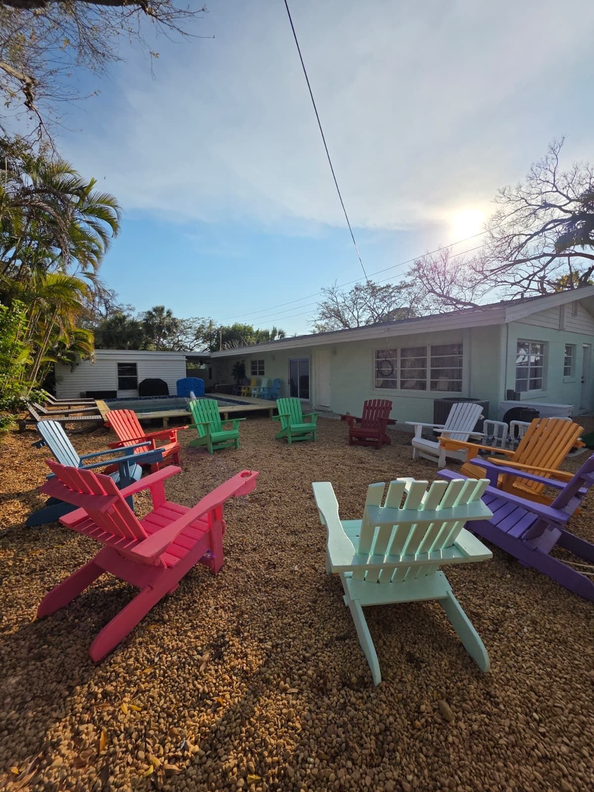 A row of colorful Adirondack chairs on a gravel surface, a building with a white exterior, and a clear sky.