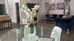 Uma sala de estar moderna com uma mesa de jantar de vidro, cadeiras brancas, um sofá azul e um ventilador de teto.