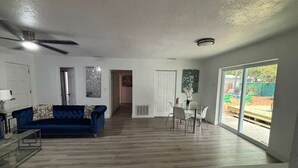 Uma sala de estar ampla, com um sofá azul, uma mesa de jantar com cadeiras e uma janela grande.