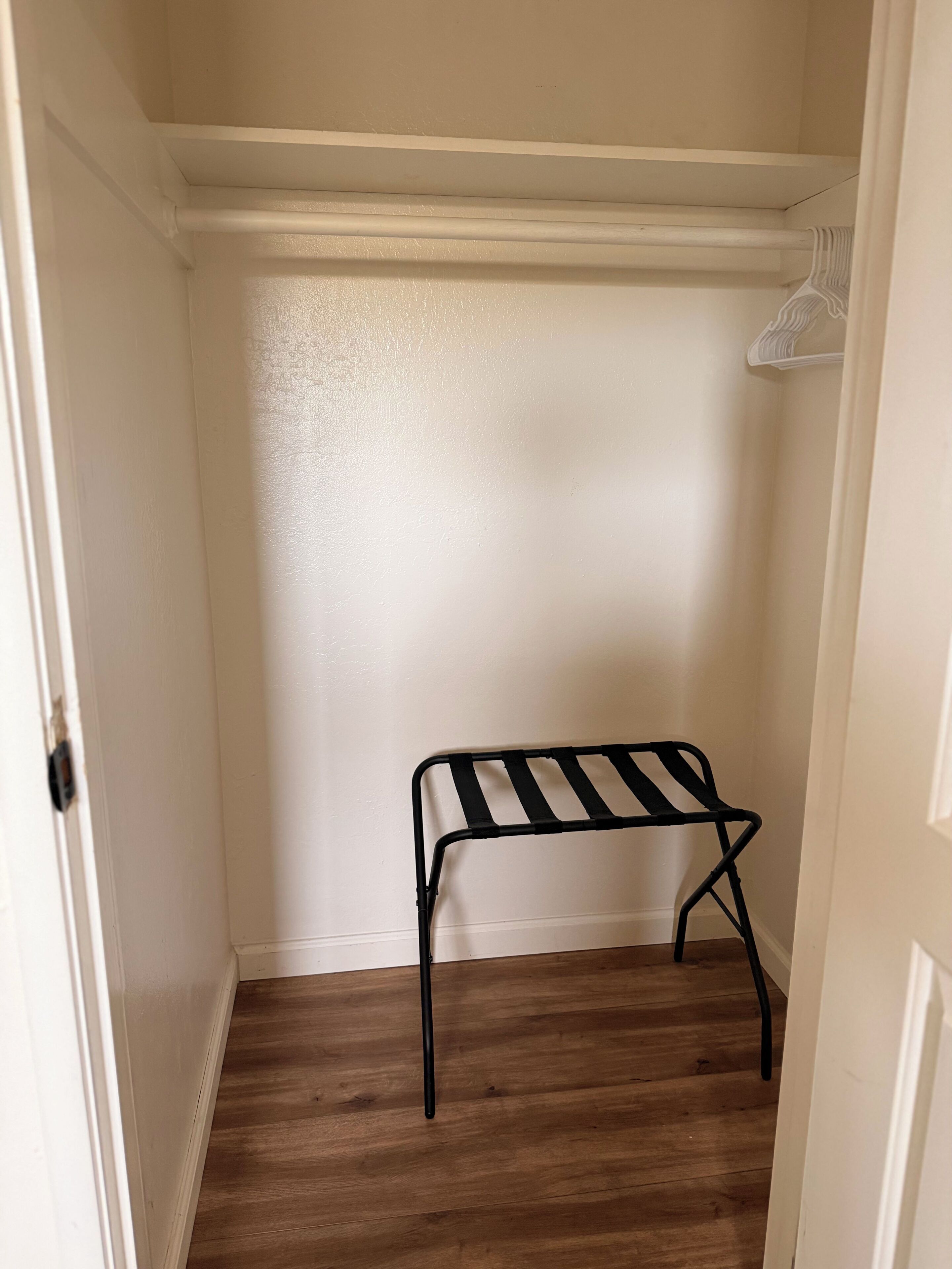 A closet with a wooden floor, a white door, and a black metal bench.